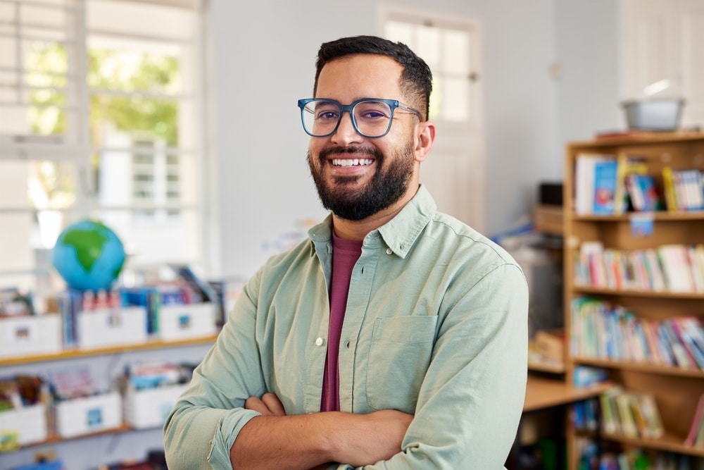 Portrait,Of,Confident,Man,Teacher,Standing,In,Elementary,Classroom,And